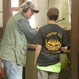A Boy Scout learning about rifles from an instructor at the rifle range